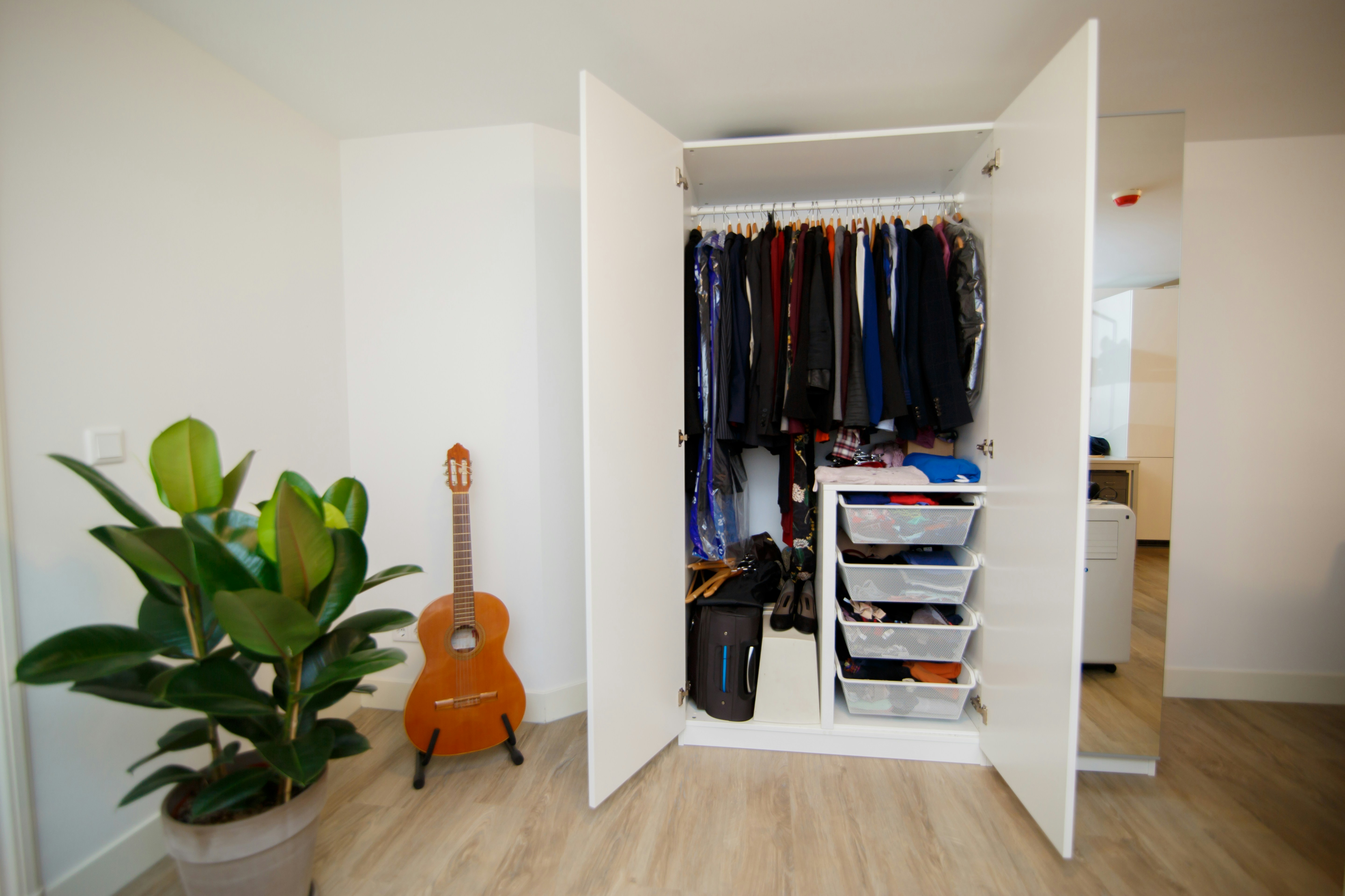 Wardrobe with hanging clothes and drawers. A bedroom with closet, plant and guitar.